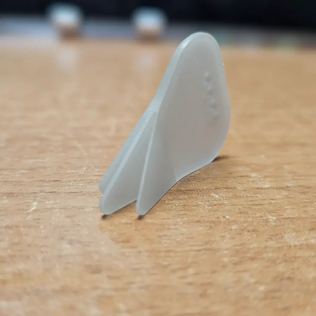 A matte white Nylon Trident pick photographed at an angle, its three tines clearly separated.