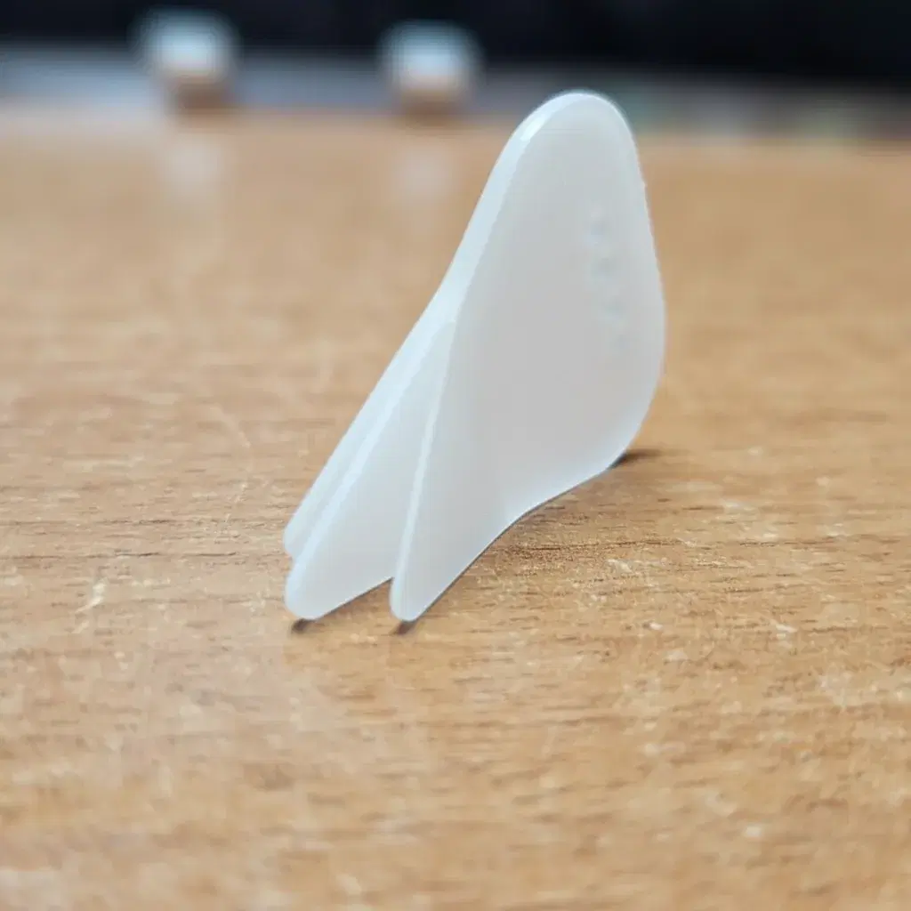 A translucent POM Trident pick shown three-quarter on, highlighting the moulded grip dimples.