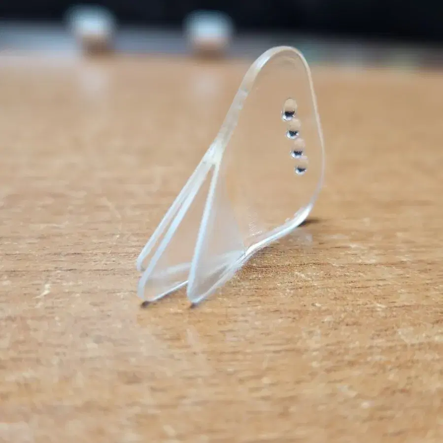 A clear Acrylic Trident pick, light refracting through its three transparent tines.