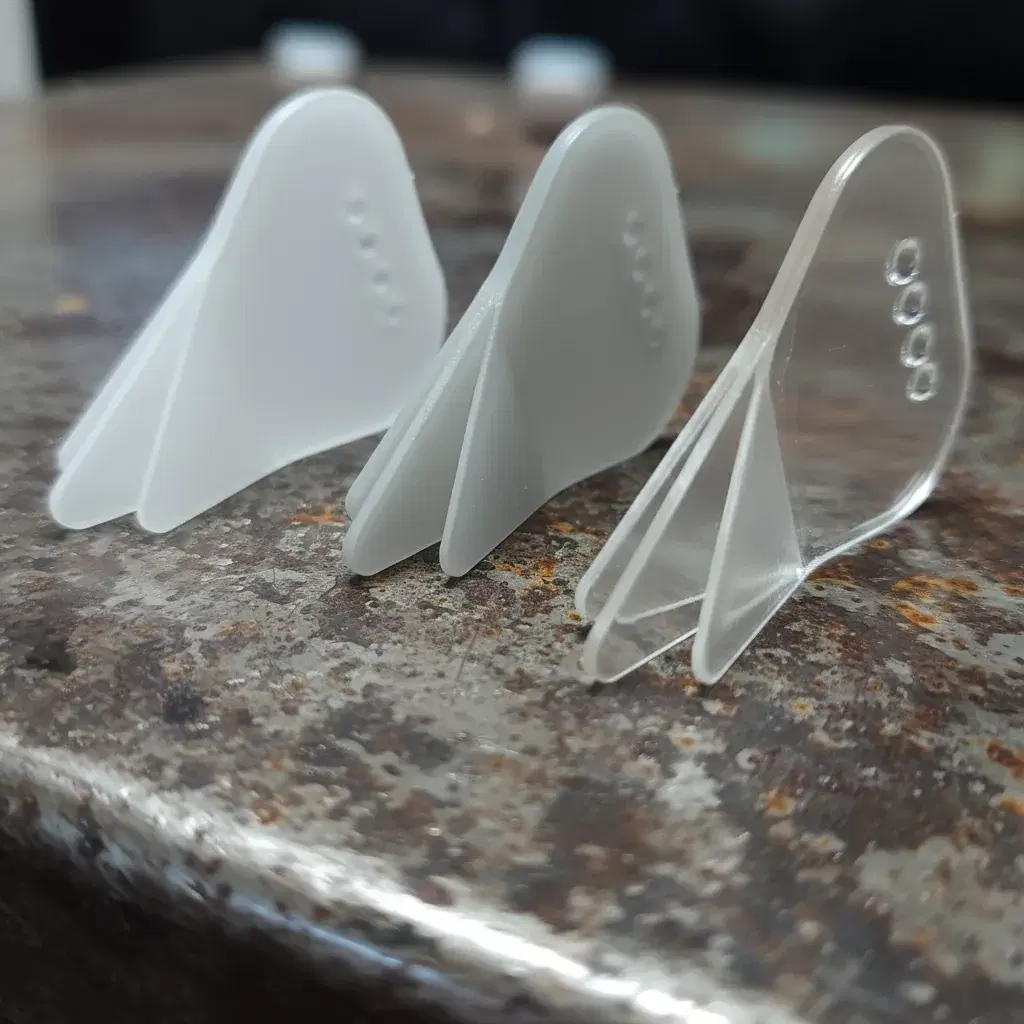 Three Trident picks standing upright, showing the Nylon, Acrylic and POM finishes side by side with their three tines fanned out.
